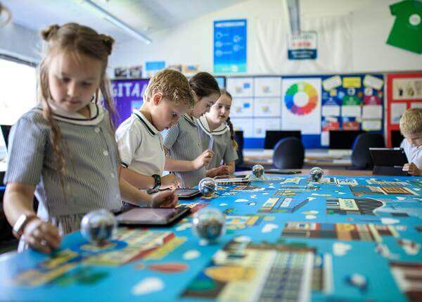 Students exploring coding activities on the Sphero Code Mat with tablets and robots in a classroom setting.