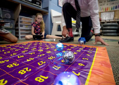 Students learning computer science with Sphero robots on a colorful grid mat in an engaging classroom setting.