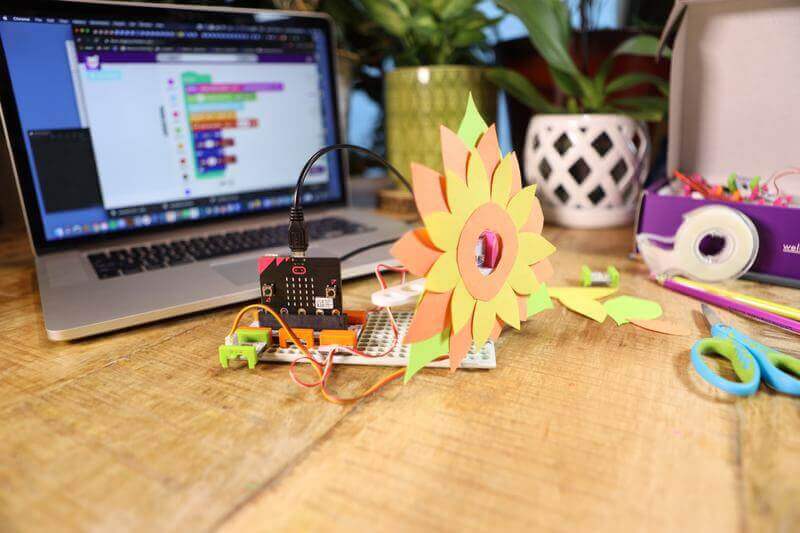 Colorful flower model made with Sphero Craft Kit, displayed next to a laptop with coding software and crafting materials.