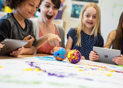 Excited children and a teacher engaged in creative learning with art projects and tablets, showcasing collaboration.
