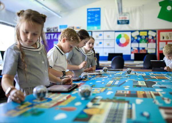Students engaged in hands-on learning at a colorful table in a classroom, using tablets and coding tools.