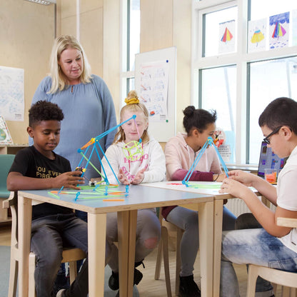 Students engaged in a STEAM activity constructing projects with Strawbees, guided by a teacher.
