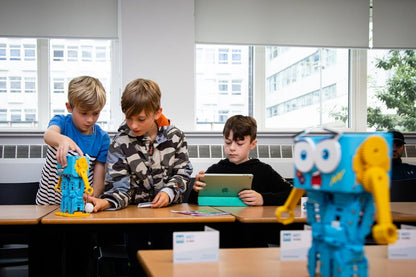Three children engaged in coding and robotics with Marty V2 robots at a classroom table.