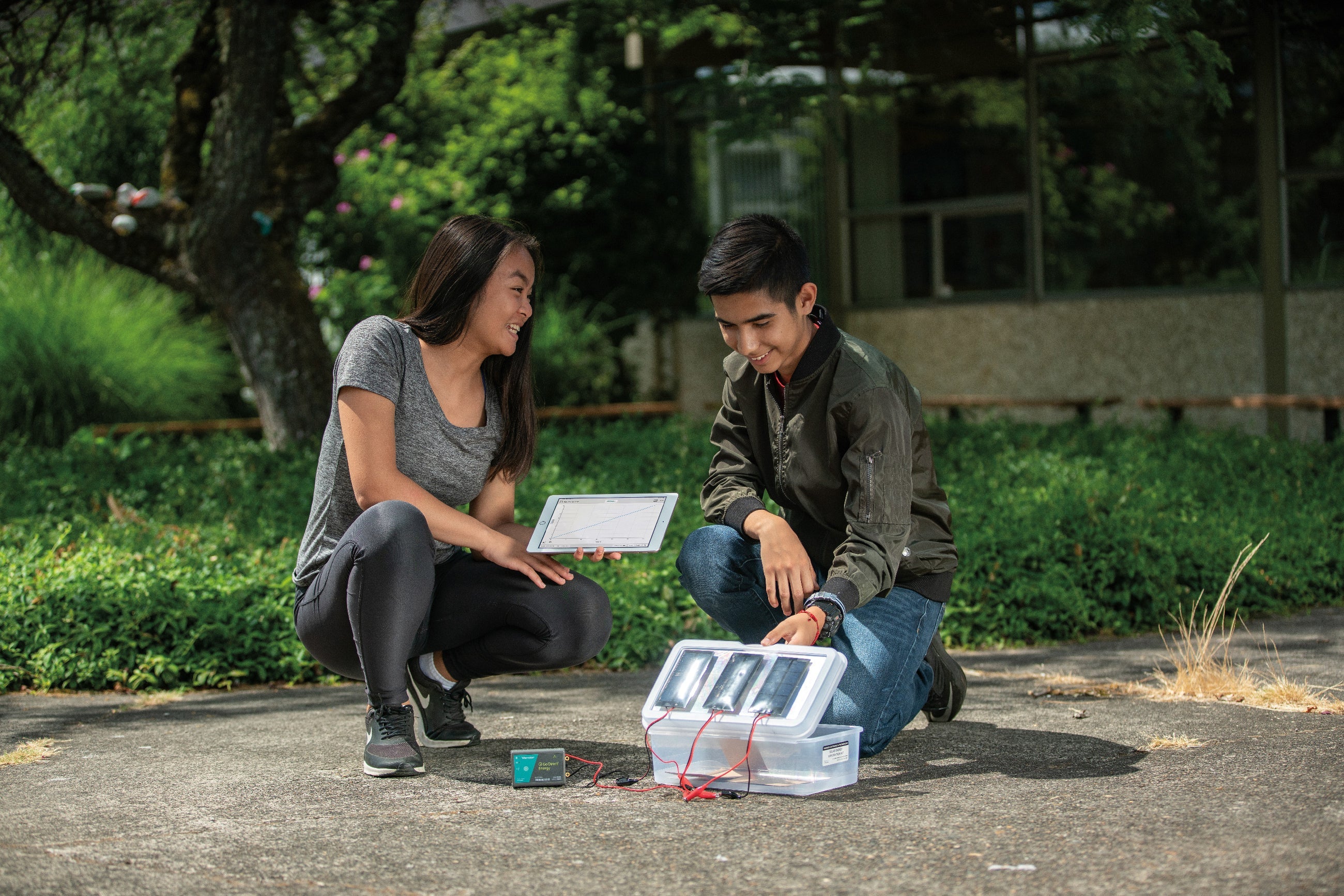 Two students experimenting outdoors with a tablet and equipment, engaged in practical learning.