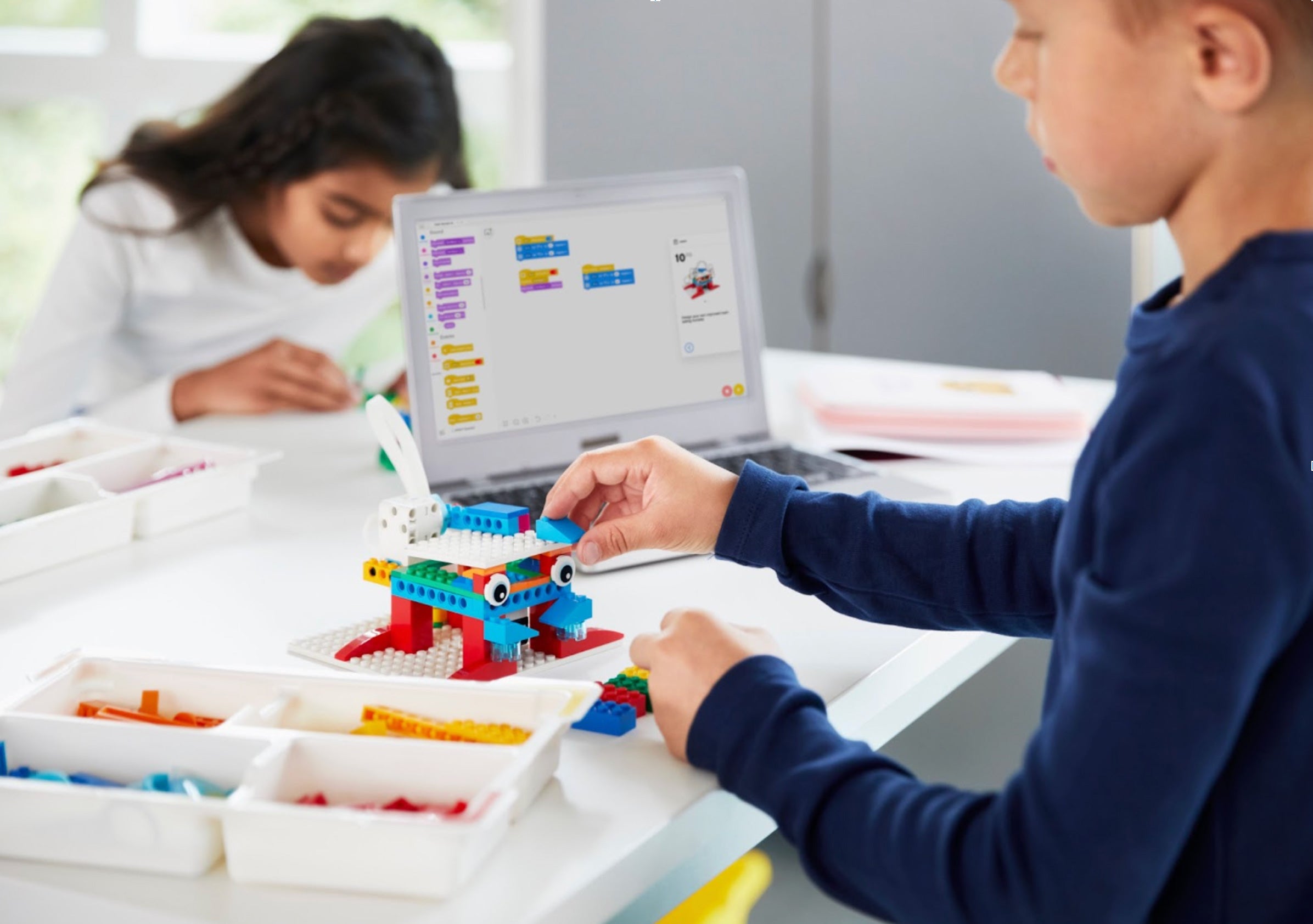 Children engaged in imaginative play with LEGO blocks, programming on laptop in a creative learning environment.